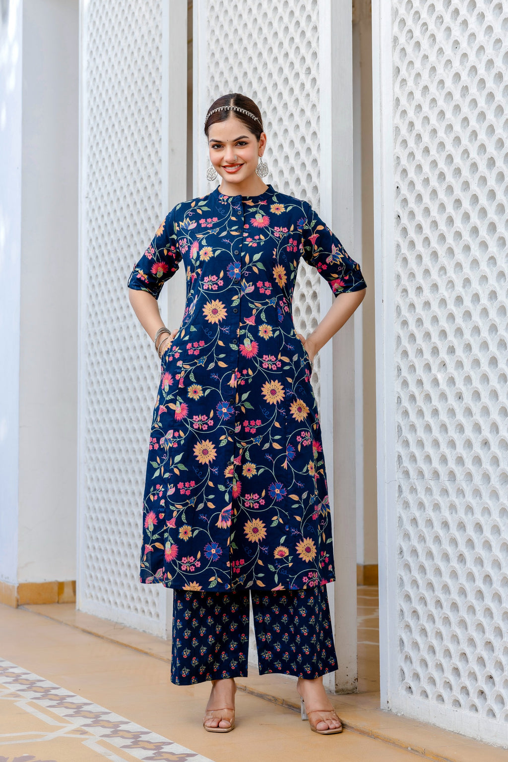 Woman wearing a navy blue floral dress standing in front of a textured white wall.