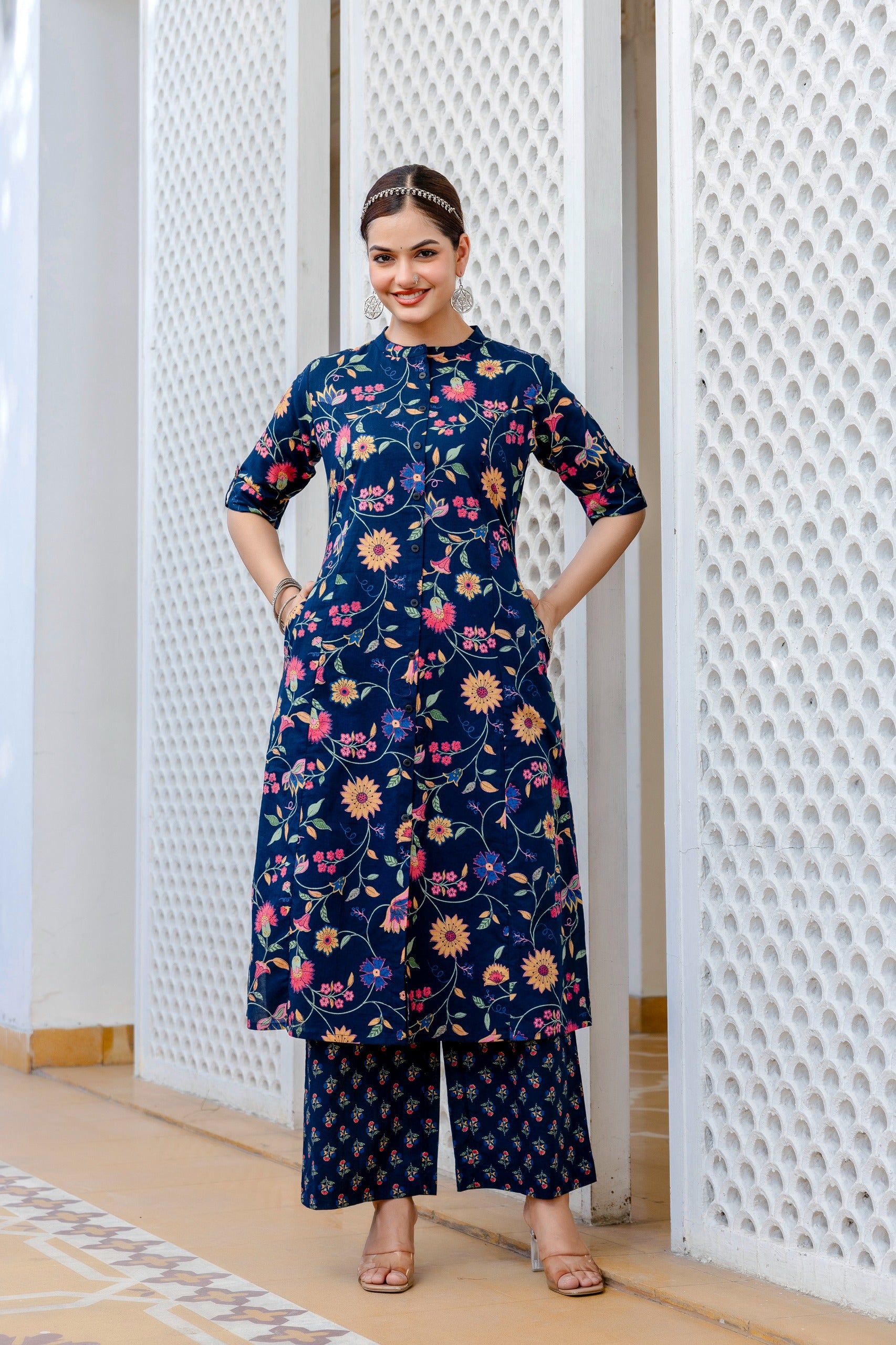 Woman wearing a navy blue floral dress standing in front of a textured white wall.